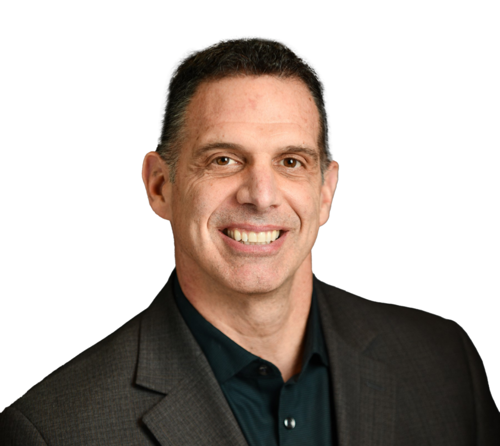 Professional headshot of a smiling man with short dark hair, wearing a dark gray suit jacket over a black button-down shirt,