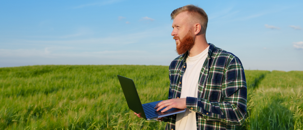 Person using a laptop in a farm field, representing farm business management, financial planning and technology solutions for agricultural operations.
